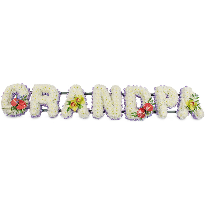 A beautifully crafted sympathy tribute fills the frame, the word "GRANDPA" presented in bold, upright capital letters, all joined together on a single horizontal frame against a simple white background. Every letter is formed from tightly massed white chrysanthemums, the petals layered like tiny feathers so the surface looks soft yet substantial, as if you could rest your hand on it. Around the base of each letter, a trim of lavender or soft lilac ribbon peeks out, its gentle hue echoing the quiet, reflective mood of a funeral or celebration of life. The supporting bars behind the letters are dark green, mostly hidden but visible enough to hint at the sturdy mechanics that allow this tribute to travel from a flower shop in Old Ford to a church near Mile End or a service by the green spaces around the Hertford Union Canal. Vivid clusters of accent flowers are placed with care: to the left, the "G" carries a spray of deep red anthuriums with their characteristic glossy, heart-shaped blooms and prominent yellow spadices, nestled in rich green foliage with touches of purple detail. The central "D" mirrors this passionate red note, creating a gentle rhythm across the arrangement. On the first and final "A", yellow-green orchids unfold in elegant sprays, their fresh colour suggesting life and cherished memories amidst the sorrow. The overall composition feels balanced and thoughtful, a personalised floral message that honours a grandfather's role in the family and offers a comforting, graceful presence at a farewell service in the Old Ford community.