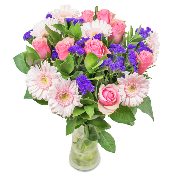 A vibrantly arranged bouquet from Old Ford is presented in a minimalist clear glass vase, placed against a pristine white background. At the centre, approximately seven to nine soft- to medium-pink roses catch the eye, their petals either tightly furled or just beginning to spiral open in classic rose formation. These sit harmoniously among five to seven pale pink gerbera daisies, each with large, welcoming faces and lighter, creamy centres, their petals radiating in delicate layers. Scattered throughout are vivid clusters of purple statice, whose deeper colour and textured, almost papery detail serve as a striking counterpoint. Lush, verdant foliage emerges from the base, providing rich depth and an abundance that echoes the nearby green corridors criss-crossing Old Ford. The transparent vase reveals fresh, water-laced stems, completing the natural tableau and suggesting a bouquet just delivered from a local atelier. This thoughtfully-constructed arrangement-pink roses, gerberas, and purple accent flowers-is perfect for marking birthdays, anniversaries, Mother's Day, or as a colourful accent in an Old Ford office or home. Its artistry and freshness convey a sense of joy, gratitude, and lasting affection, all with a distinctly local touch.